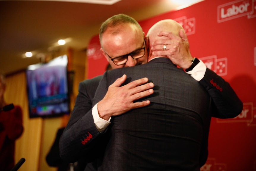 Two men in suits embrace.