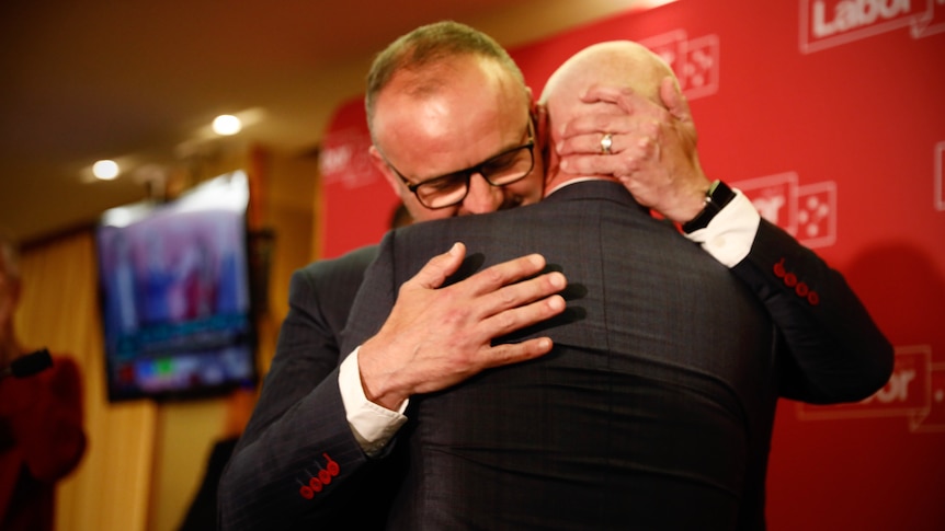 Two men in suits embrace.