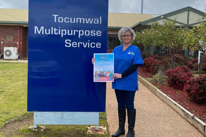 A woman in blue scrubs standing next to Tocumwal hospital sign.