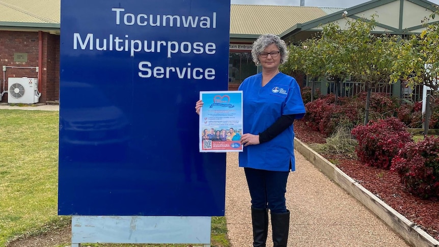 A woman in blue scrubs standing next to Tocumwal hospital sign.