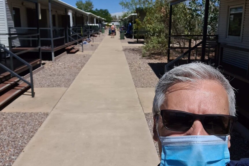 David Desira takes a selfie wearing a blue face mask with a view of the lodgings in the Howard Springs facility.
