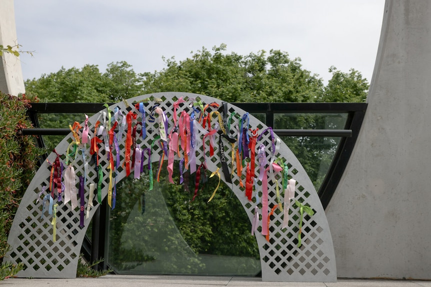 a silver lattice archway with rainbow ribbons tied