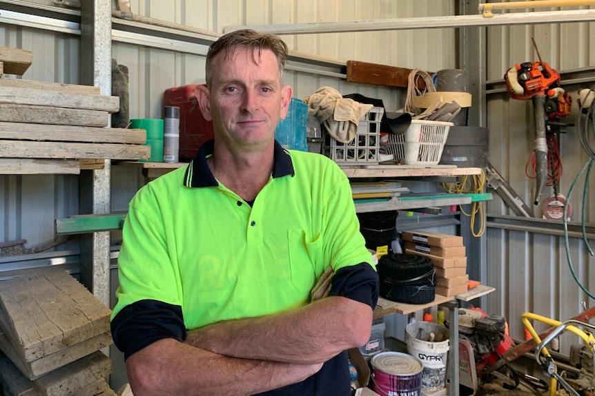 Simon stands with his arms crossed in his shed.