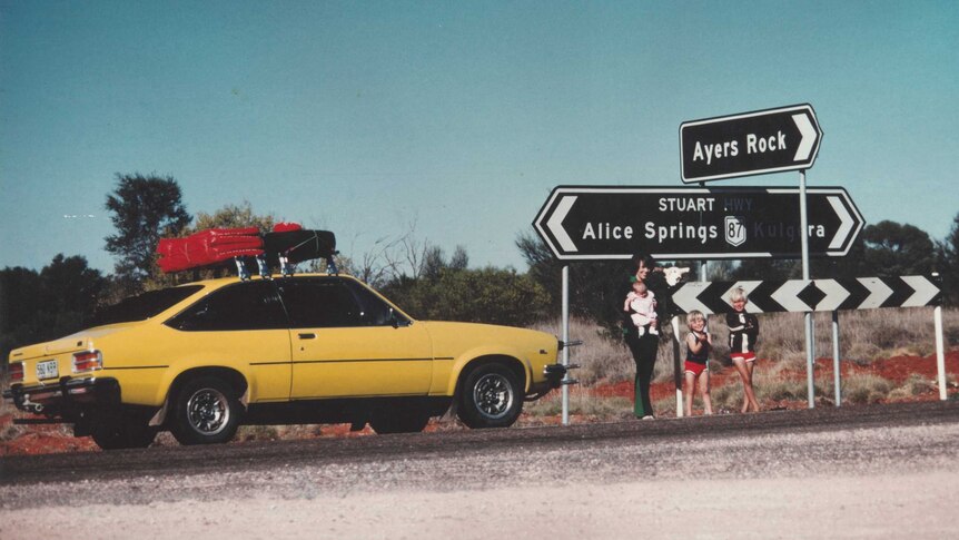 Lindy Chamberlain holding Azaria Chamberlain, with Aidan and Reagan Chamberlain, standing on the Stuart Highway with sign to Ayers Rock, alongside their Torana on August 16, 1980.