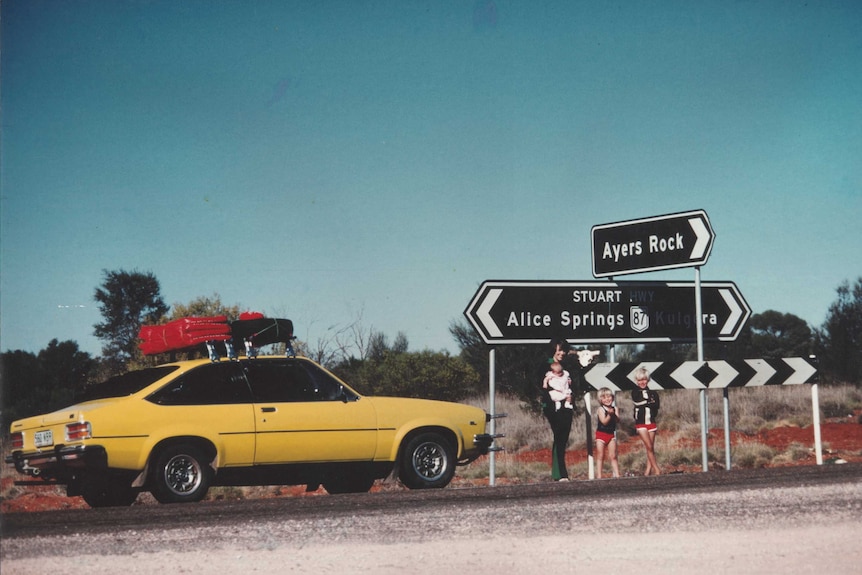 Lindy Chamberlain holding Azaria Chamberlain, with Aidan and Reagan Chamberlain, standing on the Stuart Highway with sign to Ayers Rock, alongside their Torana on August 16, 1980.