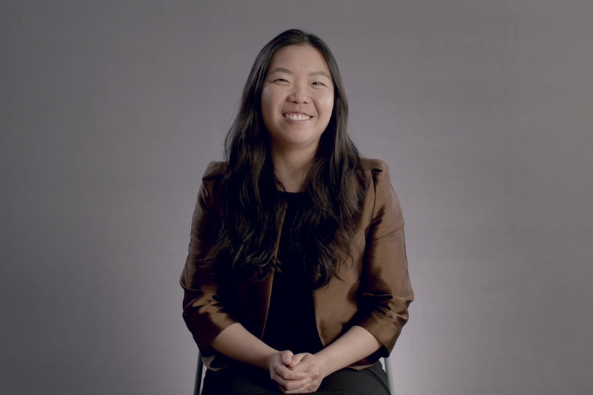 Trudy is a young Asian woman with long dark hair. She is wearing a brown jacket and is smiling.