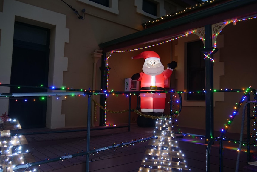 A blow up Santa Claus is illuminated and surrounded by fairy lights.