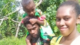 A Ni-Vanuatu mother and father walk together outside with child on his shoulders