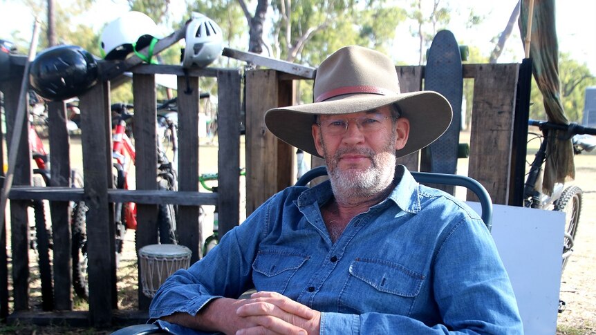 A man in a blue shirt and an Akubra hat sits in a camping chair