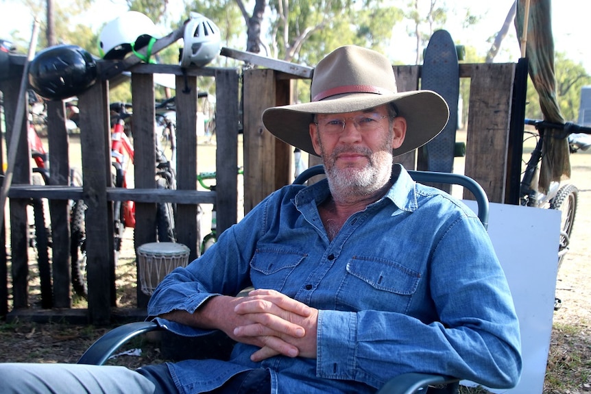 A man in a blue shirt and an Akubra hat sits in a camping chair