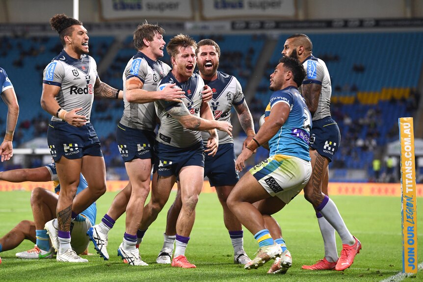 Melbourne Storm players celebrate near the corner flag after scoring a try, as Gold Coast Titans struggle to their feet. 