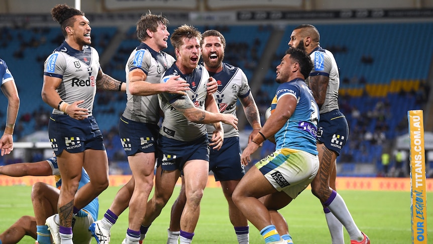 Melbourne Storm players celebrate near the corner flag after scoring a try, as Gold Coast Titans struggle to their feet. 