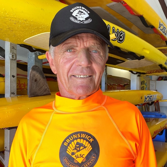 A man in his 60s looks at the camera surrounded by surfboards