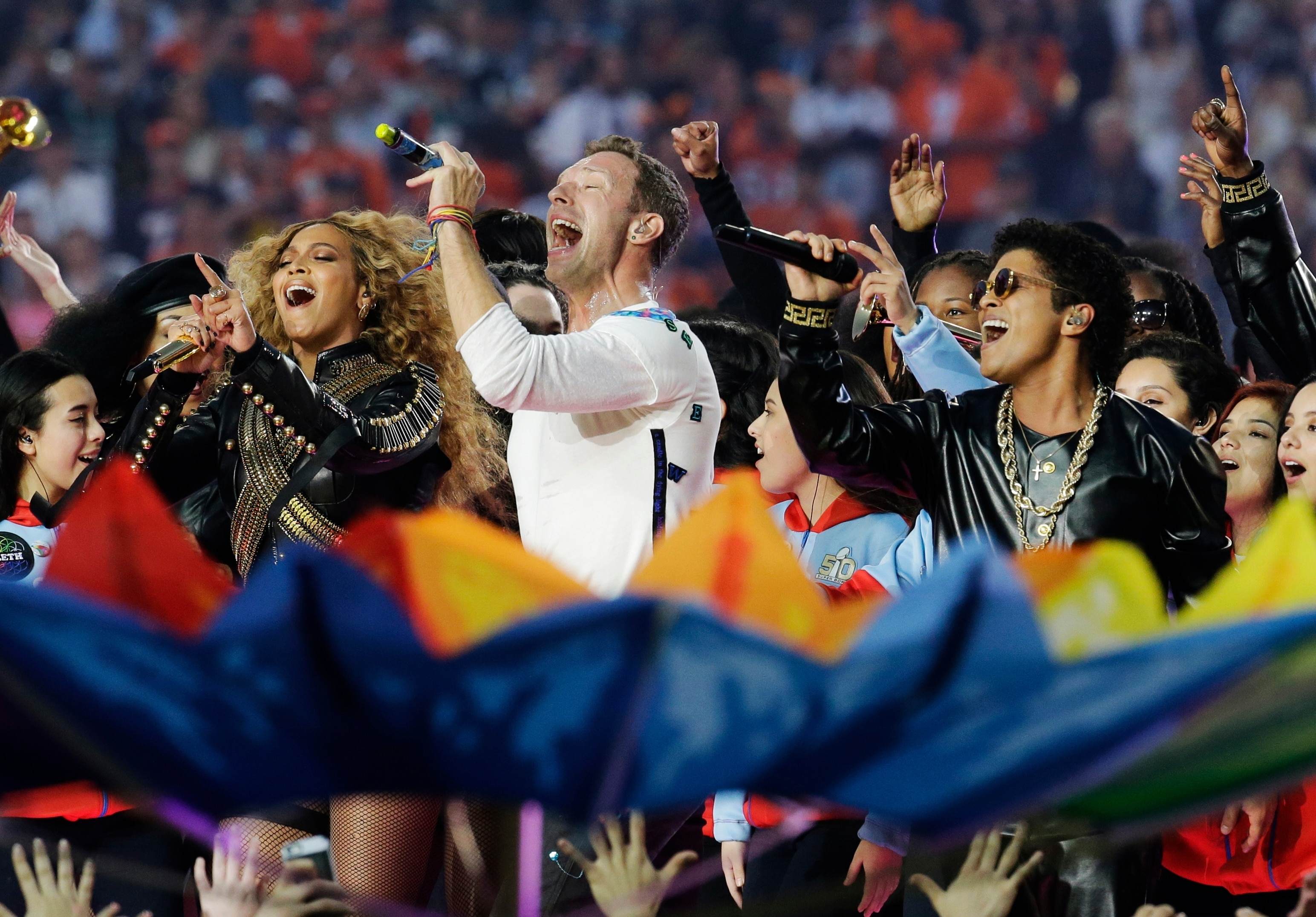Beyoncé, Chris Martin e Bruno Mars cantam no palco com uma bandeira de arco-íris