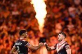 Sydney Roosters' Daniel Tupou and Angus Crichton fist bump as pyrotechnics ignite behind them.