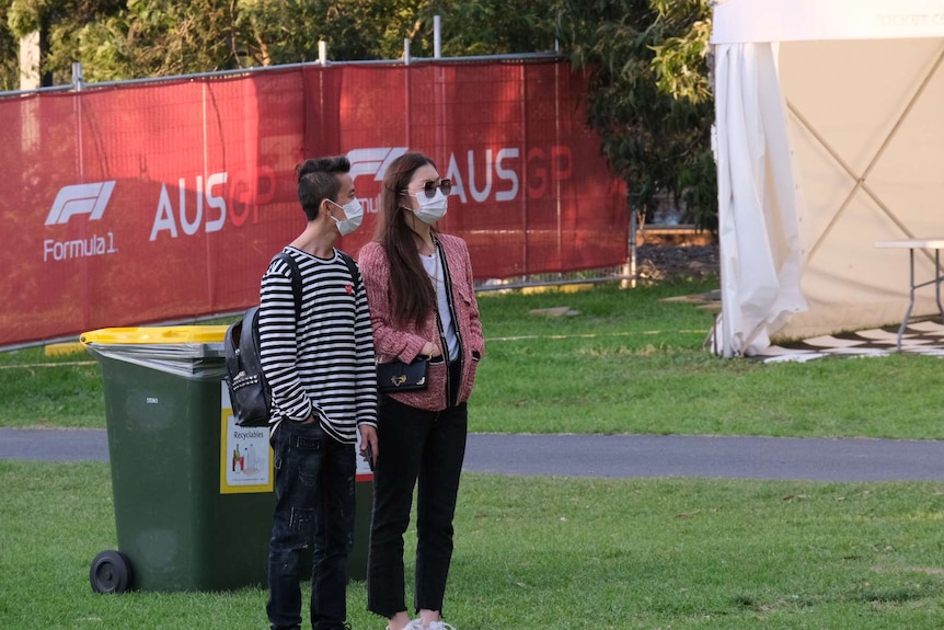 A man and woman wearing surgical masks stand outside at the Australian F1 Grand Prix.