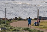 A couple looks out to Gulf St Vincent as a man runs passed at West Beach, Adelaide.