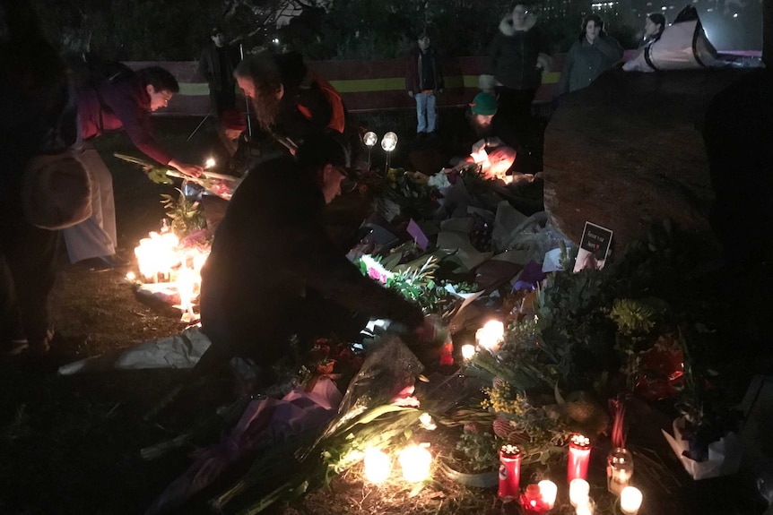 Five people in a dark park putting candles and flowers on the ground.