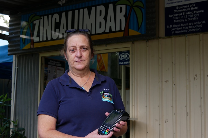 Une femme se tient devant un pub tenant une machine EFTPOS