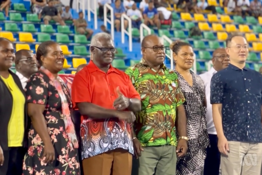 A group of Pacific men and women wearing colourful clothes pose for a photo.