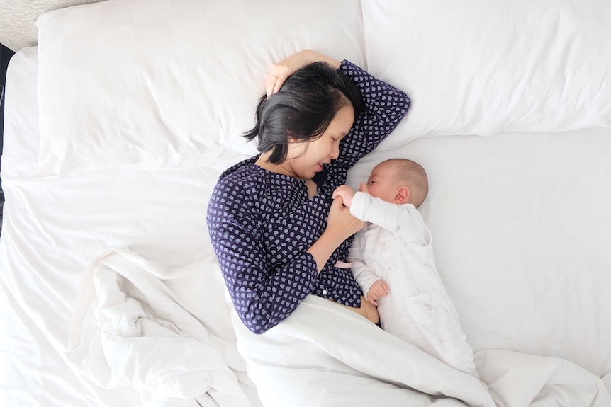 A woman lying on a bed with a small baby