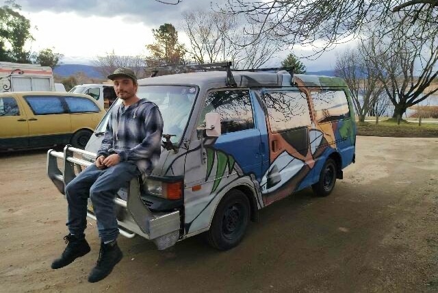 A man sits on the boot of his van at the claypits carpark.