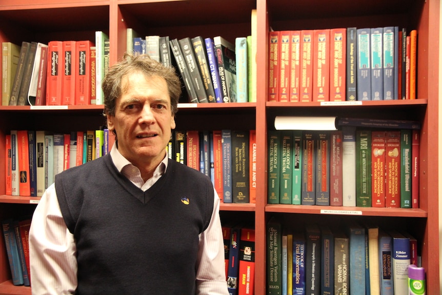 man in a long sleeve shirt and vest in front of a bookcase filled with books