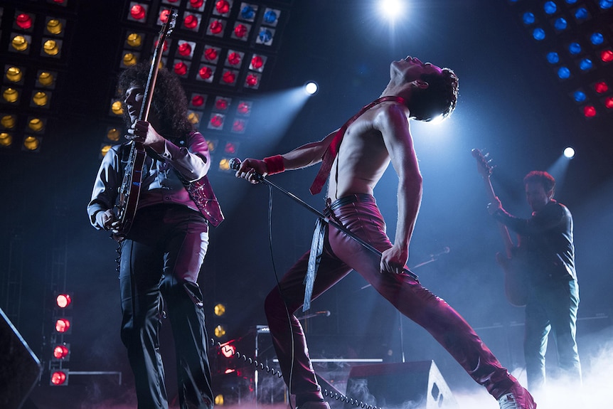 Colour still of Joseph Mazzello, Rami Malek and Gwilym Lee on stage in 2018 film Bohemian Rhapsody.