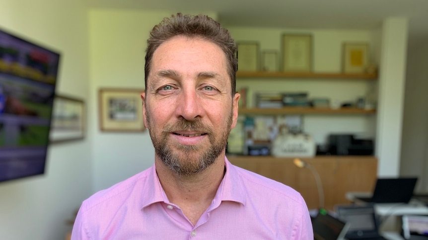 Mark Sampieri smiles, dressed in a pink business shirt inside his home office.