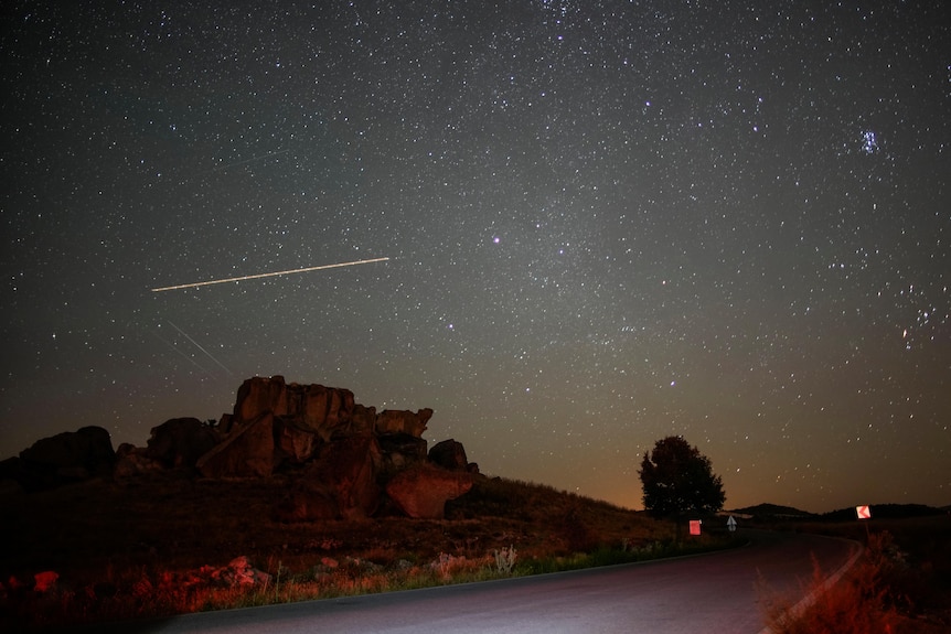 A meteor with a long white tail in the night sky with a road in the foreground