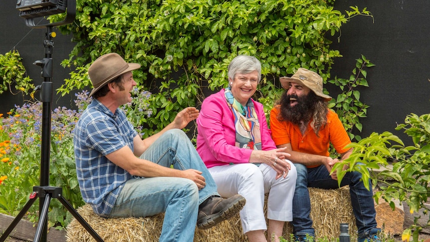 Three people sitting in garden laughing with lighting stand in shot.