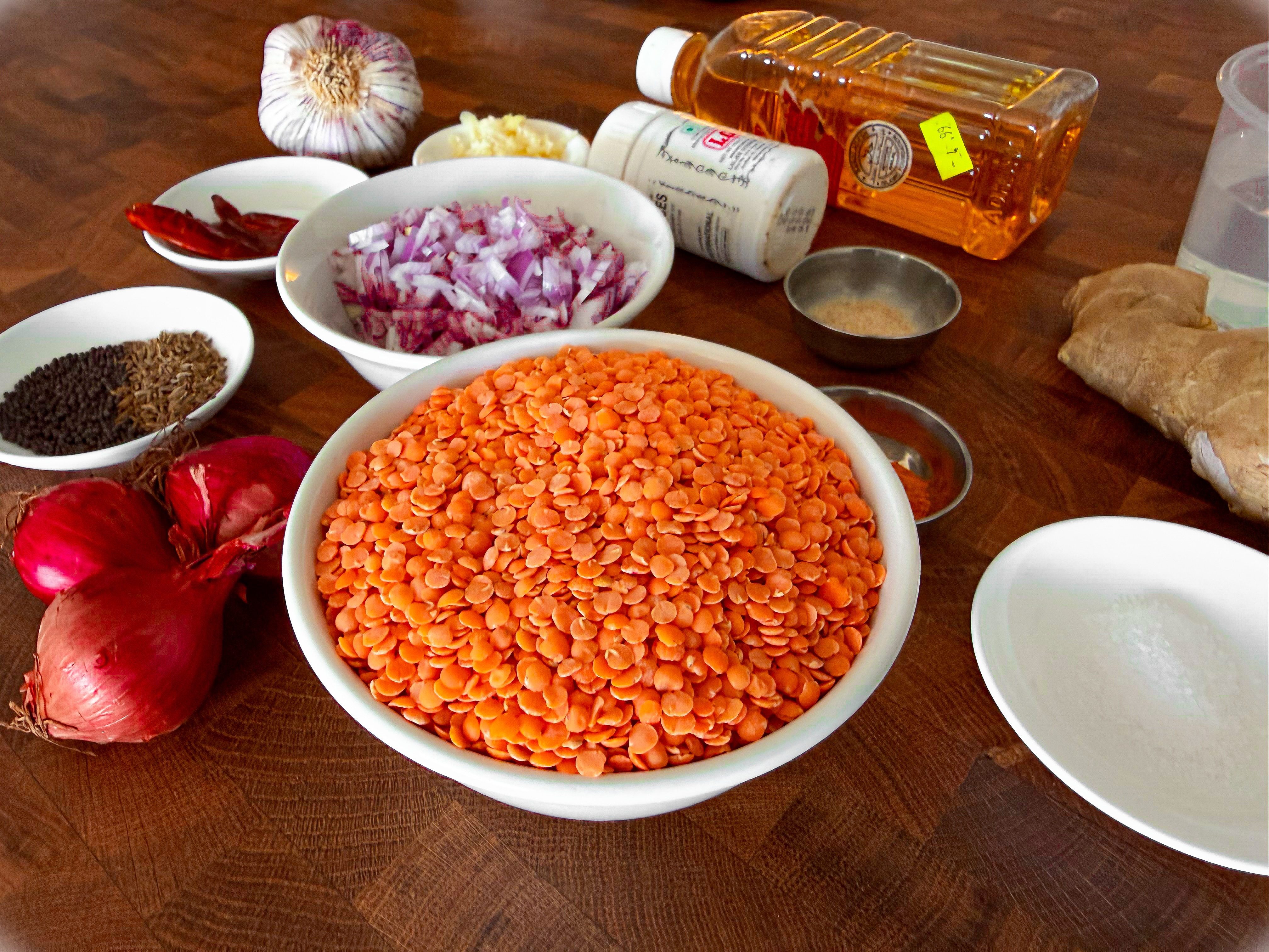 Bowls of ingredients, including red lentils, chopped onion, chilli, oil and spices, on a bench