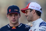 Two F1 drivers, one in blue and one in white, wearing caps, talking to each other before a race.