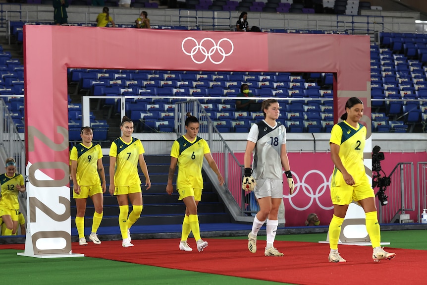 A group from Australia's Matildas walk out onto a carpet underneath a sign with the Olympic rings before a match in Tokyo.