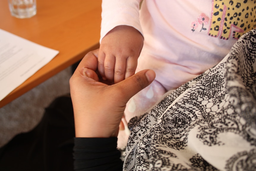 A toddler's hand holds the hand of an adult. In front of them are papers on a desk.