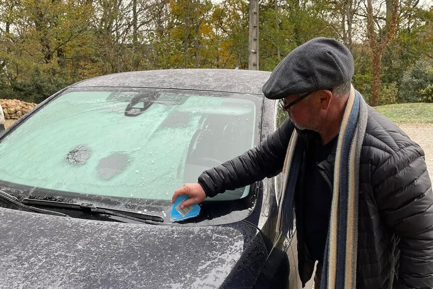 A man removes snow from the front of a car.