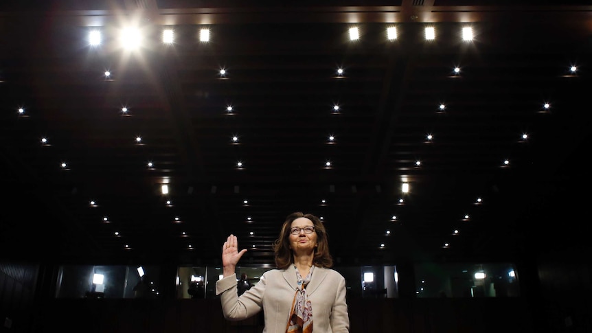 Gina Haspel holds one hand in the air as she is sworn in.