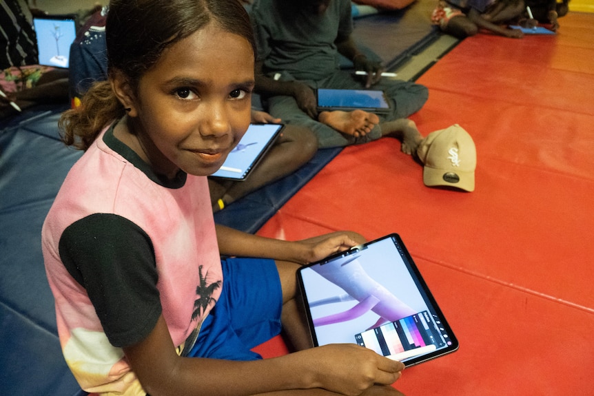 a young girl draws a design on a tablet while sitting on the floor.