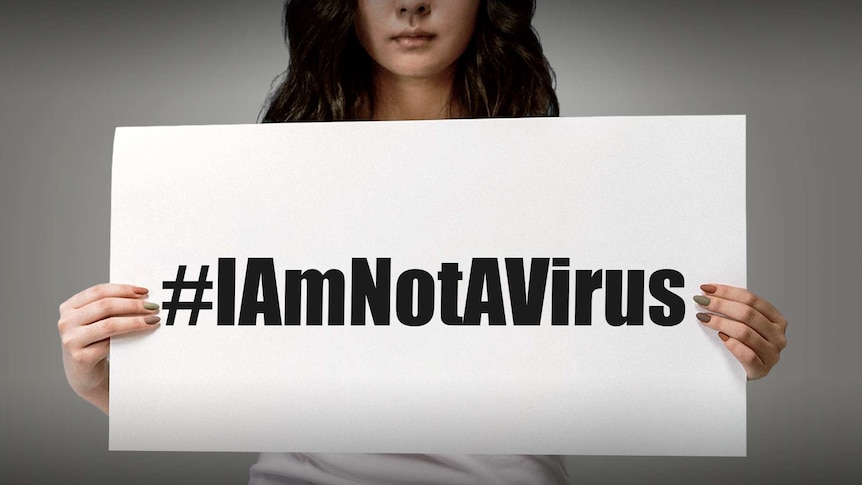 You view a woman of Asian ethnicity holding a white card that reads #Iamnotavirus