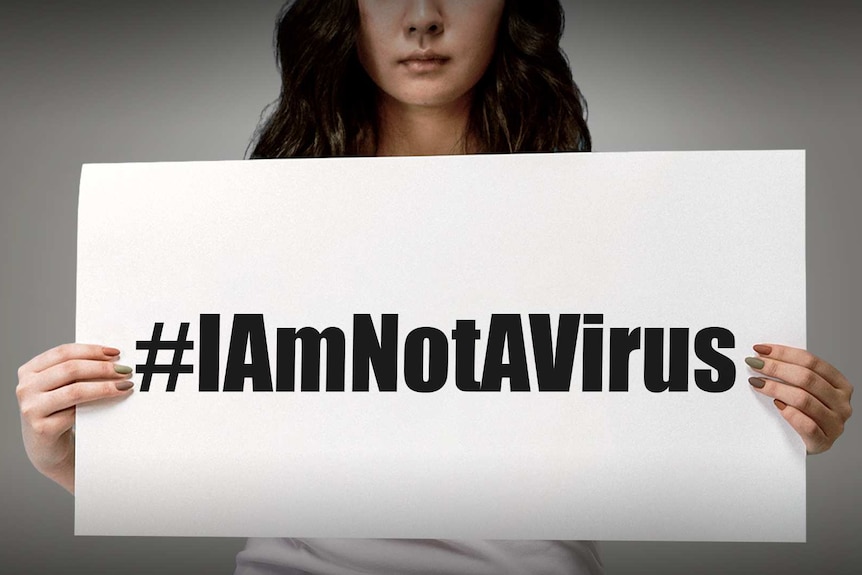 You view a woman of Asian ethnicity holding a white card that reads #Iamnotavirus