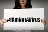 You view a woman of Asian ethnicity holding a white card that reads #Iamnotavirus