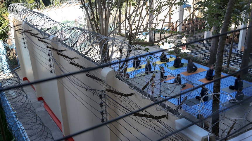 Thai women prisoners attend a yoga class behind high razor wire.