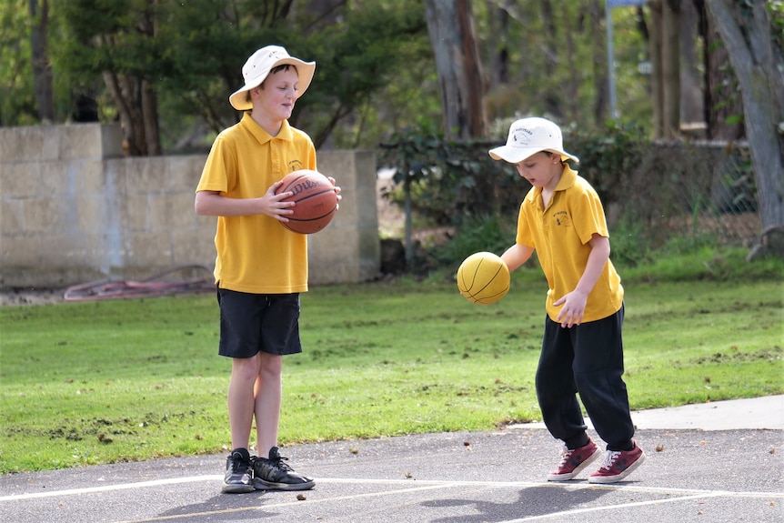 Two boys in yellow tshirts bounce basketballs.
