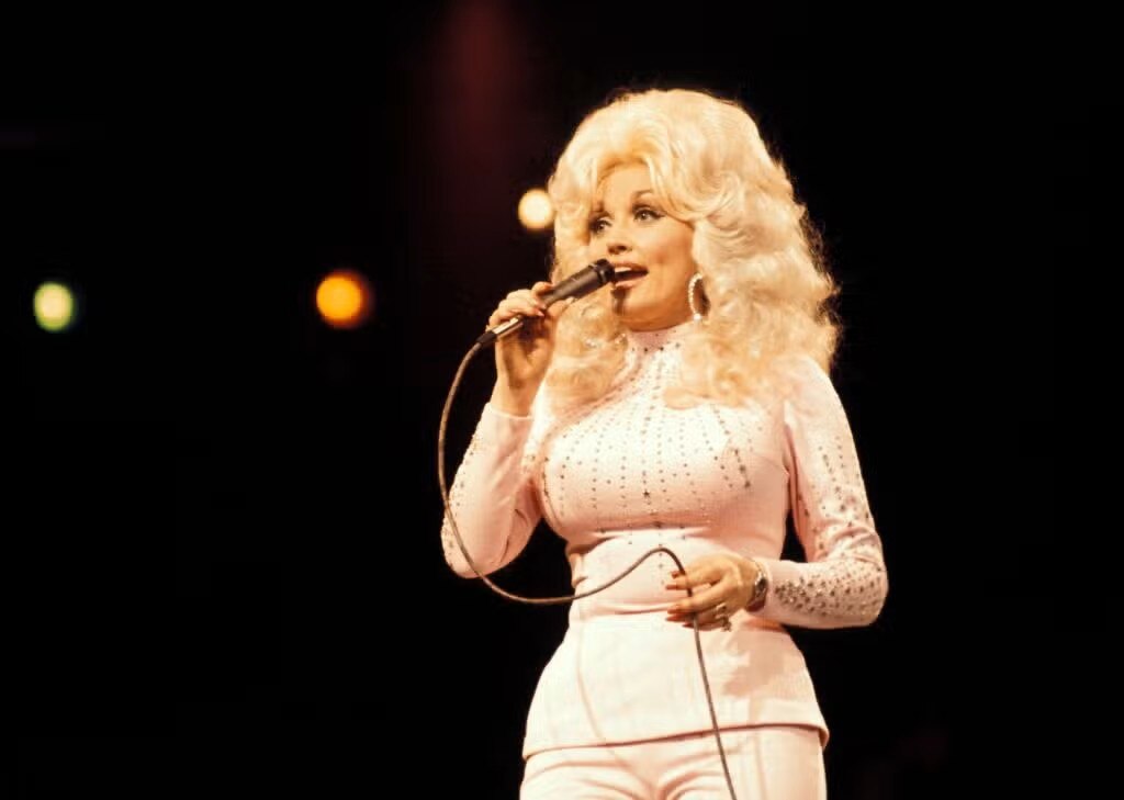 Dolly Parton in a white rhinestoned outfit singing on stage