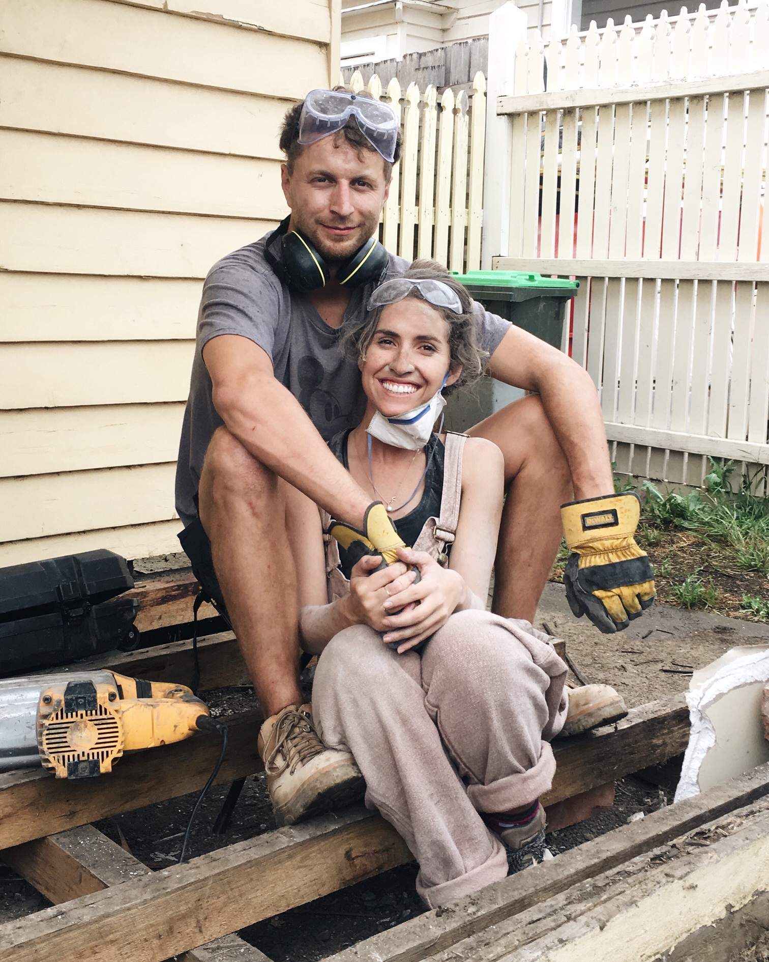 A young man and woman sitting outside a house smiling while covered in dirt from renovating to depict renovating tips.