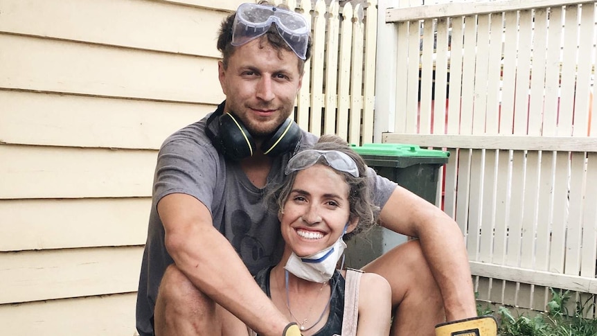 A young man and woman sitting outside a house smiling while covered in dirt from renovating to depict renovating tips.
