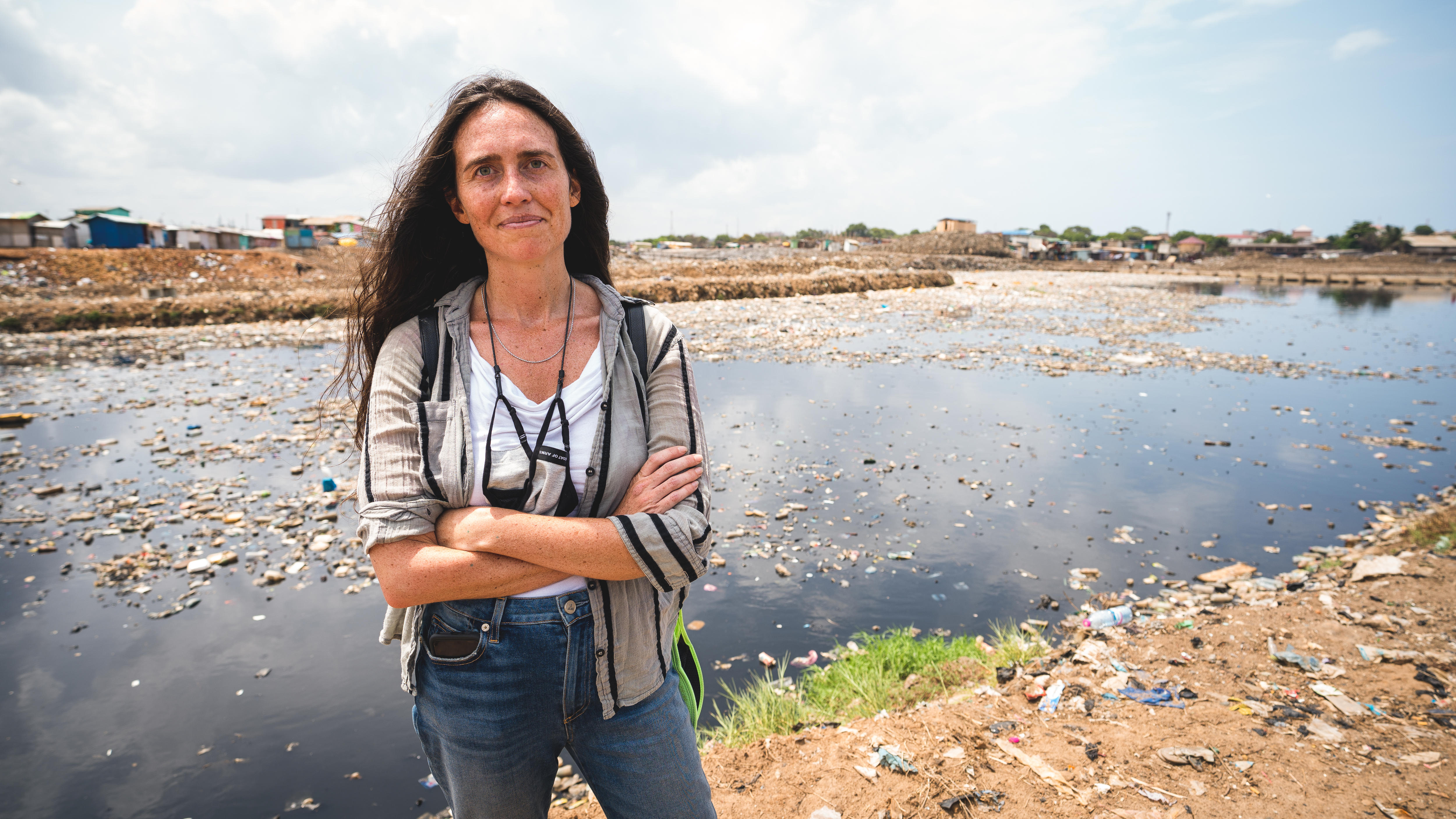 A woman stands in front of a polluted river.