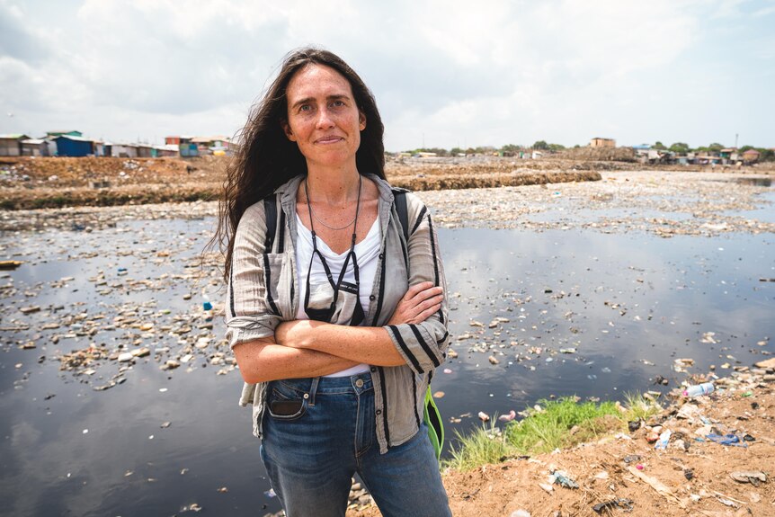 A woman stands in front of a polluted river.