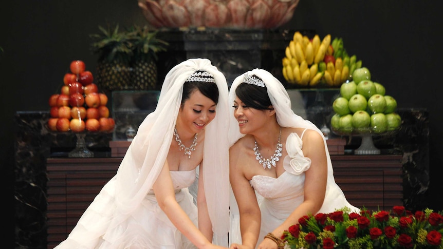 Two women wearing wedding dresses stamp their names in front of a statue of Buddha in a prayer hall.