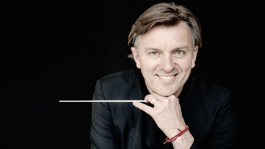 Conductor Tomas Netopil smiling at camera against a black background